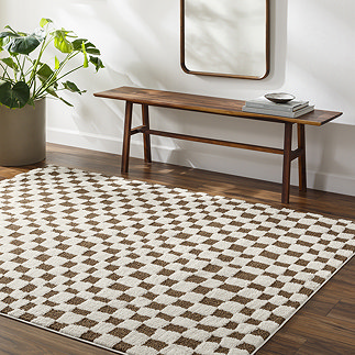 image of brown and ivory checkered rug on dark wood flooring next to walnut bench and potted plant
