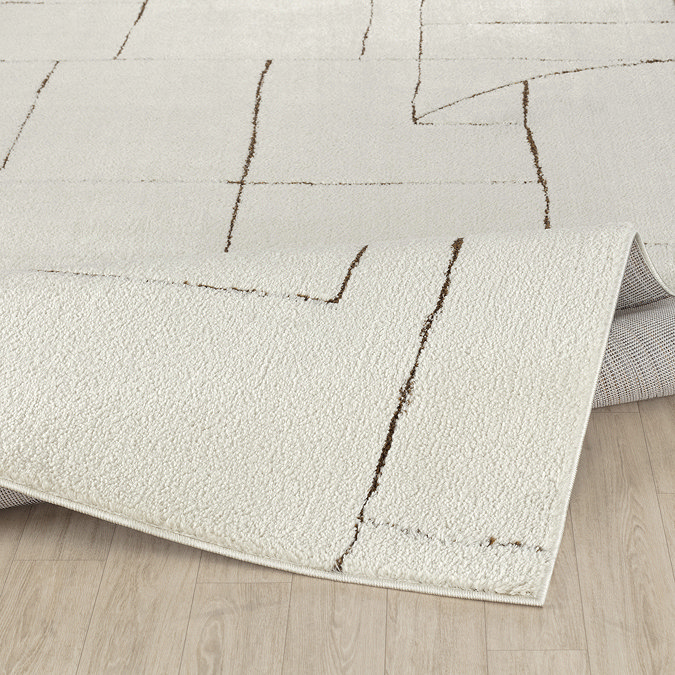 image of ivory rug with brown weaved geometric patterns, folded to suggest its thickness