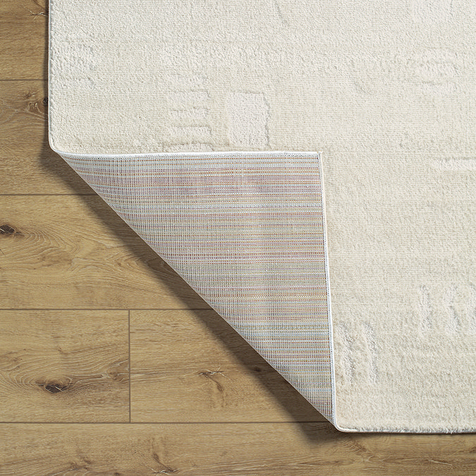 image of ivory rug with subtle geometric pattern, folded in corner to show material underneath