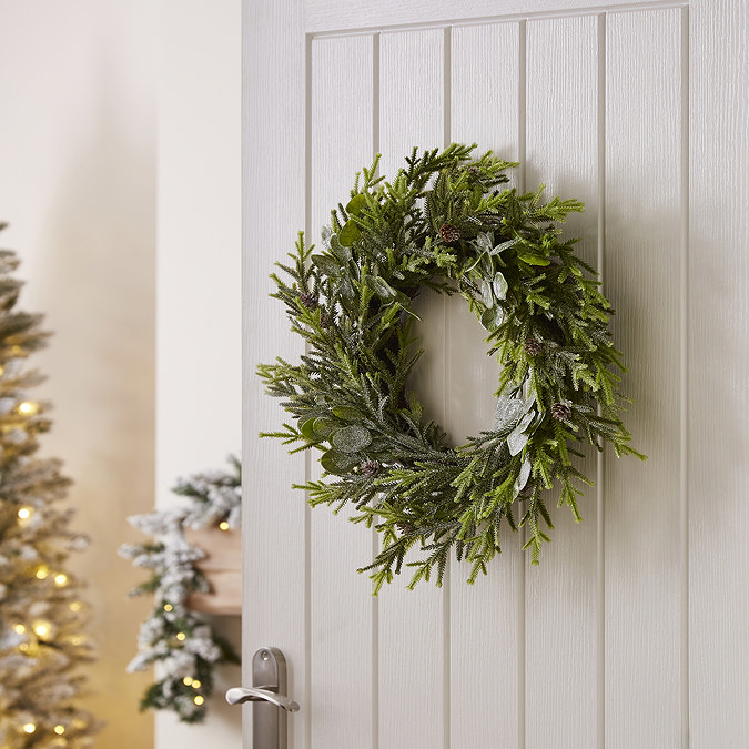 frosted pine and eucalyptus wreath hung on the back of a white living room door