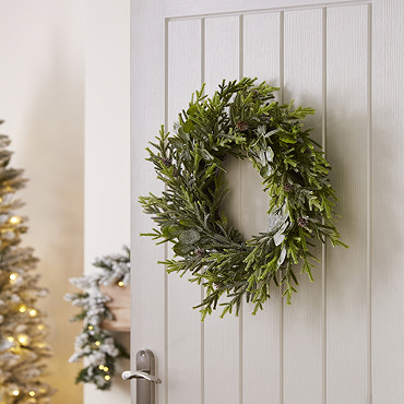 frosted pine and eucalyptus wreath hanging on a navy blue front door
