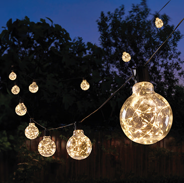 close up image of warm white glowing outdoor light, rounded shape and firefly glowing effect, in garden at night
