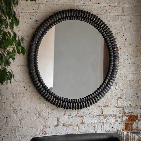 image of rounded black wooden wall mirror with textured effect on a sandstone wall