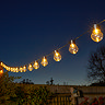 image taken at night of round bulb string lights emitting warm white light strung up between fences