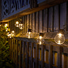 image of round warm white bulbs on fence at night, emitting a cosy glow