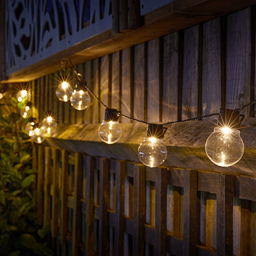 image taken at night of round bulb string lights emitting warm white light strung up between fences