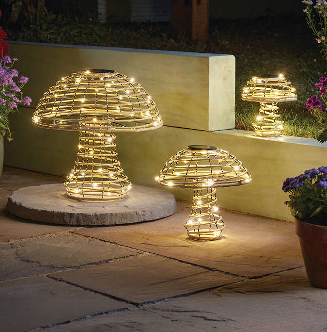 wide image of set of three rattan mushrooms with warm white lights wrapped inside them, on garden patio