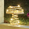 image of small rattan mushroom with small lights wrapped inside it, emitting warm glow on garden patio at dusk