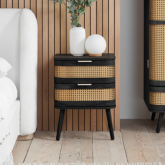 image of 2 drawer black and rattan bedside table on a wooden floor next to a white bed