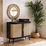 image of black two door sideboard with rattan front, against a light taupe wall with mirror hanging above it and tall faux plant to the right