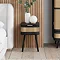 image of black bedside table with single rattan-fronted drawer on a wooden floor and topped with globe light and medium white vase