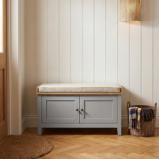 image of dark grey storage bench with two doors and metal handles, with off-white cushioned top in hallway
