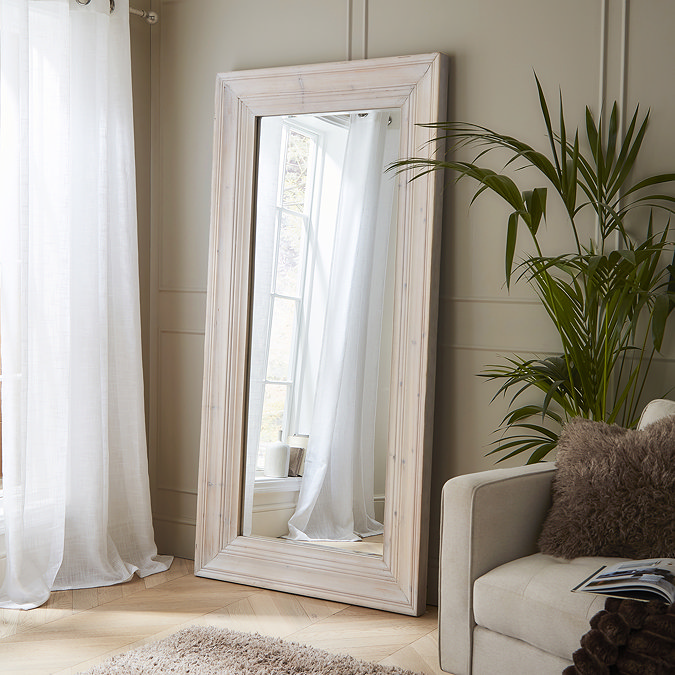 large whitewashed mirror, stood against a pale green living room wall