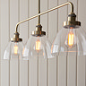close up image on clear glass light shades houses warm white filament LEDs on a three-drop linear industrial antique brass bar light