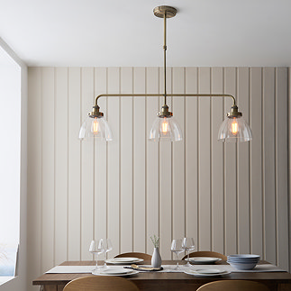 image of 3 pendant linear bar light over a dining table emitting warm light, with cream panelled wall behind