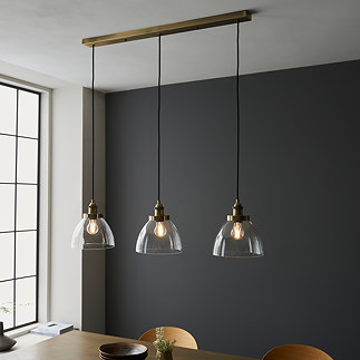 image of clear glass light shades ensconcing warm white filament LEDs on a three-drop linear industrial antique brass light fixture over a dining table