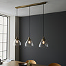image of clear glass light shades ensconcing warm white filament LEDs on a three-drop linear industrial antique brass light fixture over a dining table