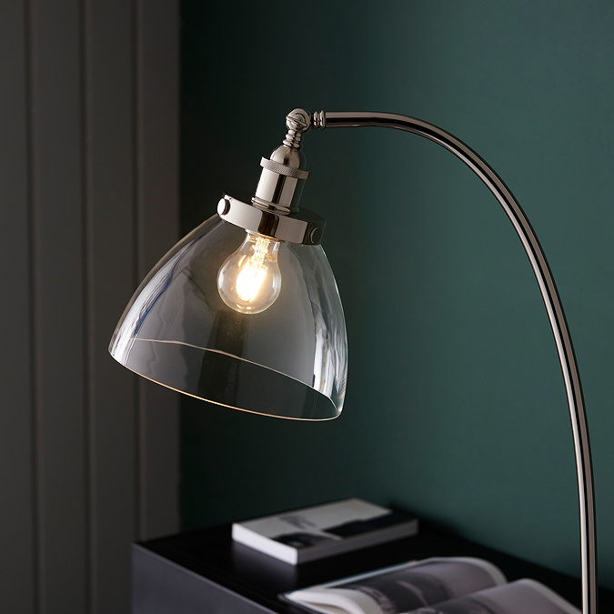 close up image of top of gently arched floor lamp in bright nickel, with clear glass shade ensconcing a warm white LED bulb