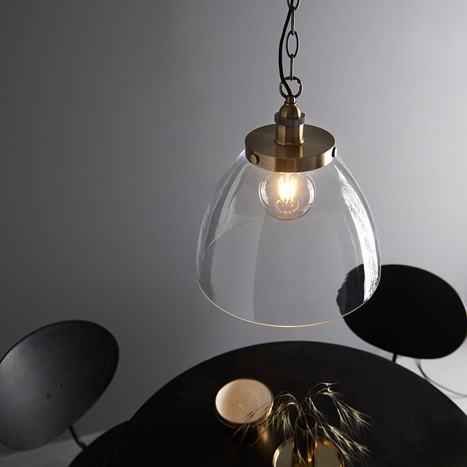 image taken slightly from above of large clear glass pendant light with antique brass fixture and large chain over black dining table