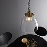 image taken slightly from above of large clear glass pendant light with antique brass fixture and large chain over black dining table