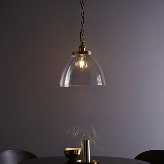 image of large clear glass light shade over warm filament bulb with antique brass fixture and hanging chain with black cable, over a dining table in front of purple wall