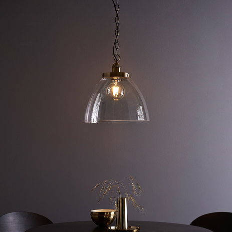 image of large clear glass light shade over warm filament bulb with antique brass fixture and hanging chain with black cable, over a dining table in front of purple wall