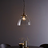 image of large clear glass light shade over warm filament bulb with antique brass fixture and hanging chain with black cable, over a dining table in front of purple wall