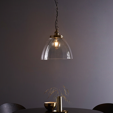 image taken slightly from above of large clear glass pendant light with antique brass fixture and large chain over black dining table
