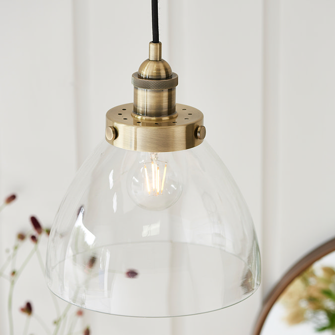 close up image of clear glass lamp shade with antique brass fixture, with warm filament bulb emitting light from within