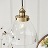 close up image of clear glass lamp shade with antique brass fixture, with warm filament bulb emitting light from within