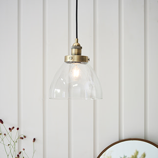 image of pendant light with clear glass shade and antique brass detail, hanging in front of cream panelled wall