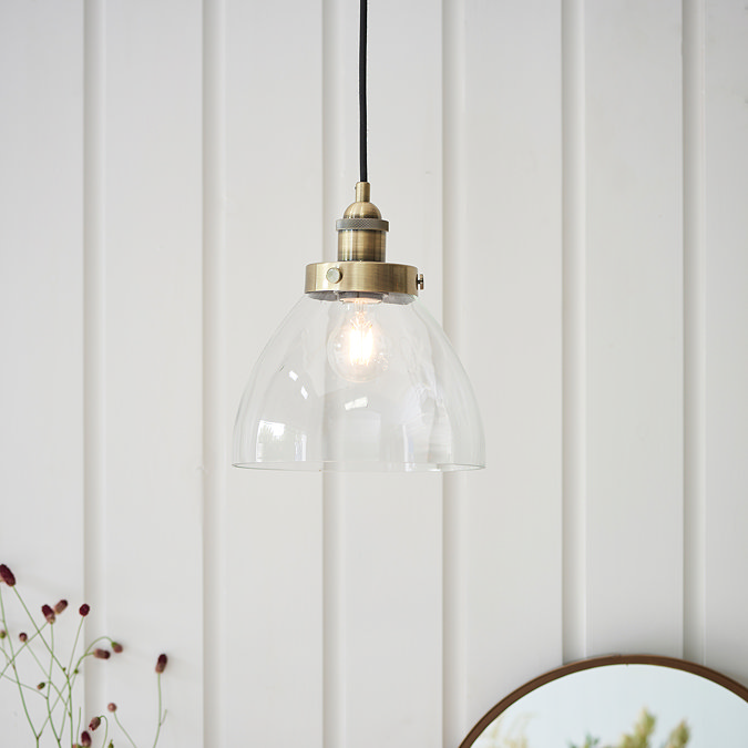 image of pendant light with clear glass shade and antique brass detail, hanging in front of cream panelled wall