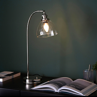 image of gently arched nickel table lamp with clear glass shade emitting warm glow over a book on a desk