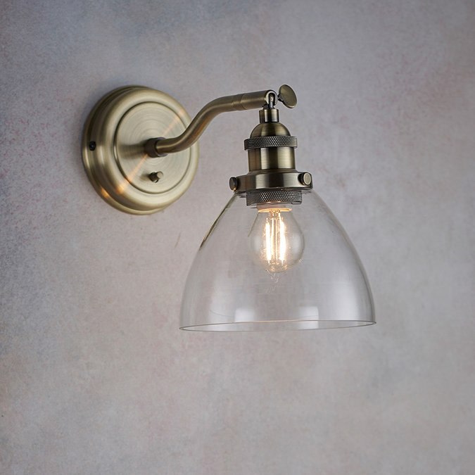 image of wall light with clear glass shade and antique brass fixture on a light purple wall