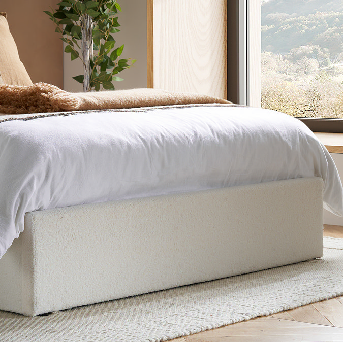 close up on bottom of ottoman bed with white base, resting on white woven rug on wooden floor