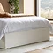 close up on bottom of ottoman bed with white base, resting on white woven rug on wooden floor