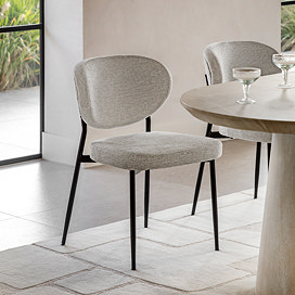 image of natural coloured upholstered dining chair with black legs and slightly curved back, on a marble floor