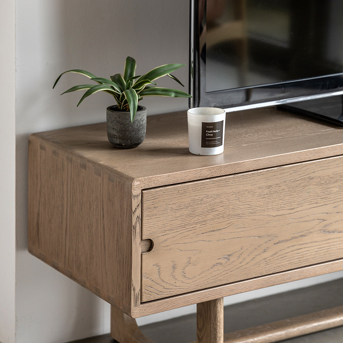 close up image of left drawer of tv unit with small cut-out handle and faux plant on top of smooth oak surface