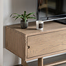 close up image of left drawer of tv unit with small cut-out handle and faux plant on top of smooth oak surface