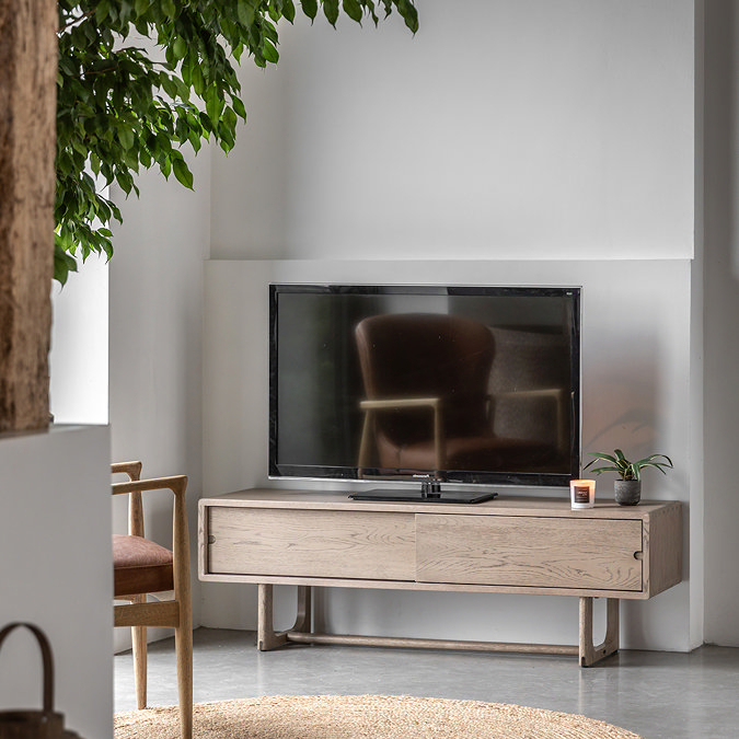 image of smoked oak tv unit with slim horizontal sliding doors and tv on top of it, with oval rug slightly out of frame