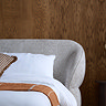 close up on rounded headboard of grey fabric bed, with plush pillows, against a dark brown wall