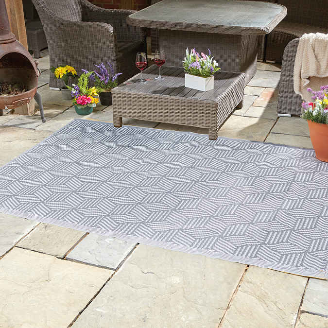 image of diagonal wavy lined slate grey rug on patio under grey rattan furniture