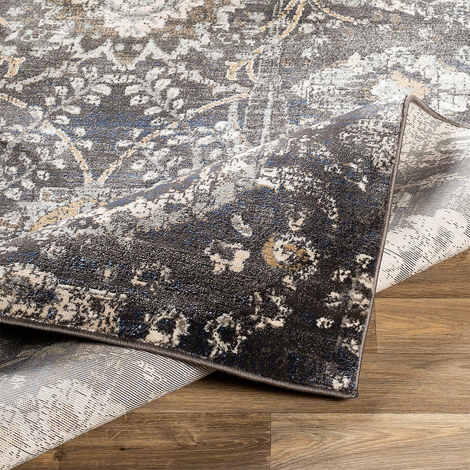 image of black rug with beige and grey floral pattern, folded slightly to reveal material underneath