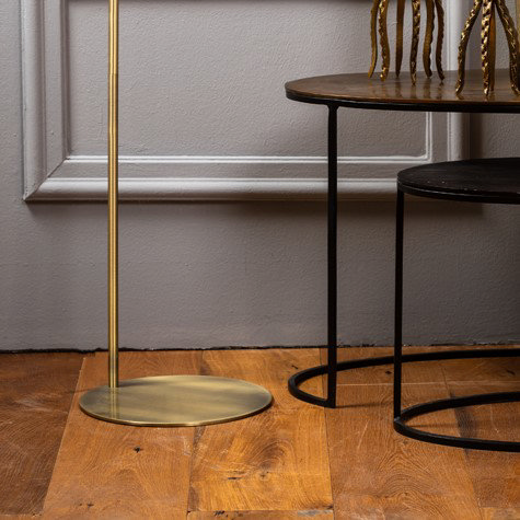 close up image on circular base of antique bronze floor lamp stood on oiled wooden flooring