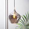 image of smoked glass pendant light with bulb inside emitting warm glow in front of grey panelled wall and potted fern