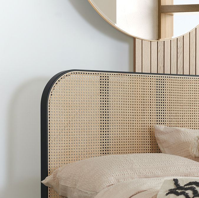 close up on rattan headboard of black framed bed with cream cushions on