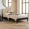 side on image of black rattan double bed with cream duvet on and black patterned cushions