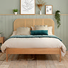 front on image of oak rattan bed with curved headboard, pushed up against sage green wall