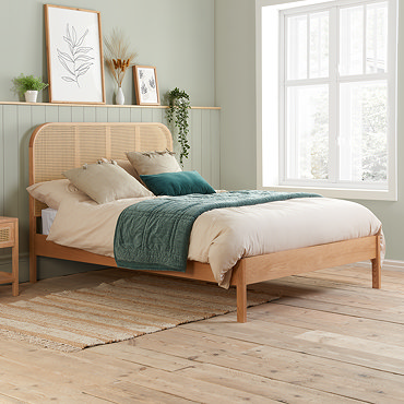 front on image of oak rattan bed with curved headboard, pushed up against sage green wall