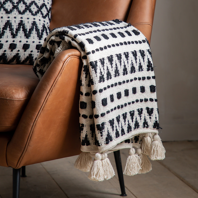 close up image of black and white geometric throw with tassel edges, draped over side of faux brown leather armchair